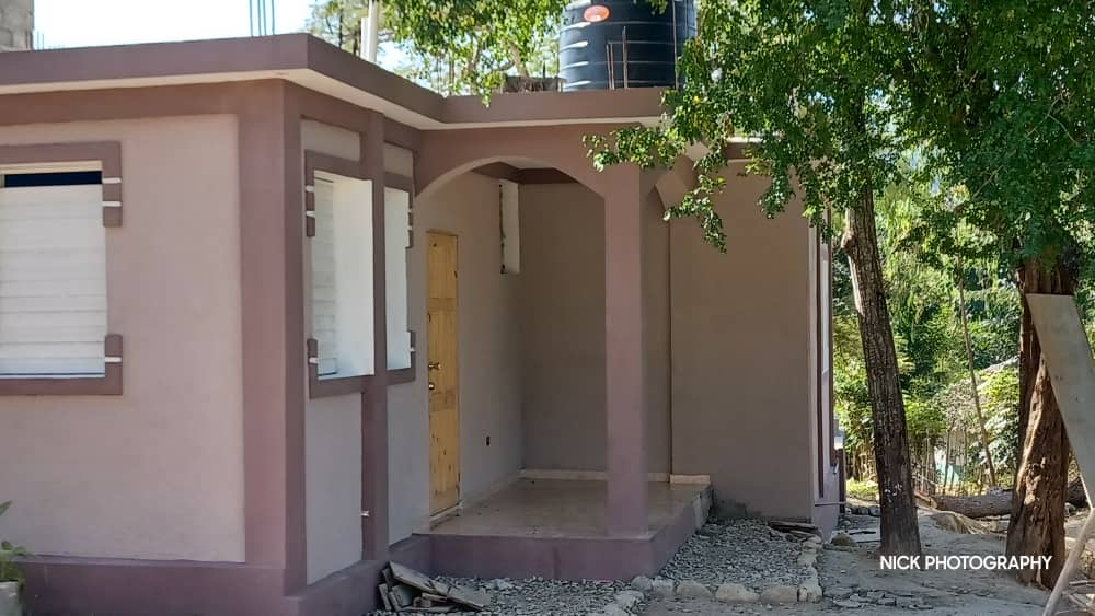 Completed presbytery exterior in Guinaudée showing the front entrance, windows, and water tank.