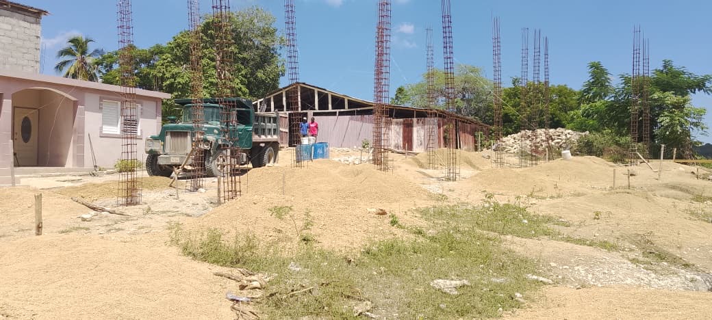 Wide view of the Sainte-Thérèse d’Avila church construction site with reinforced columns, delivered materials, and the nearby presbytery.